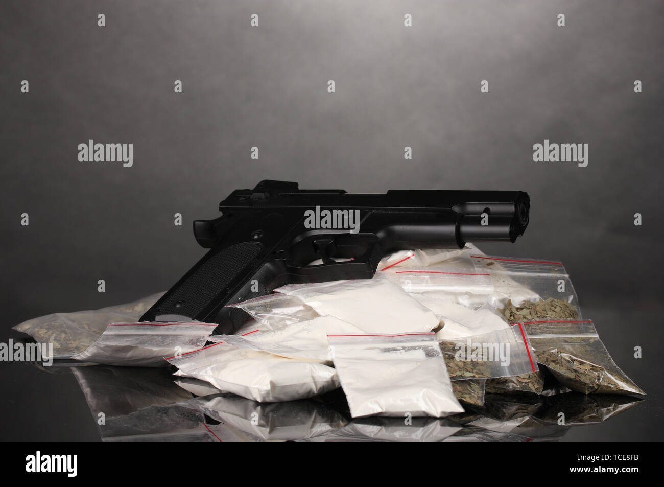 Cocaina e marijuana in pacchetti e pistola su sfondo grigio Foto Stock