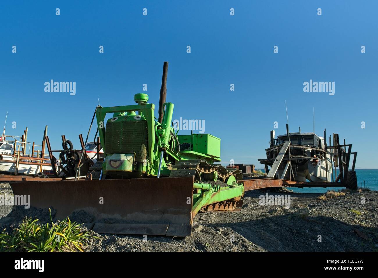 Bulldozer verde con una faccia tirando una barca fino alla spiaggia, Ngawi, Nuova Zelanda. Foto Stock