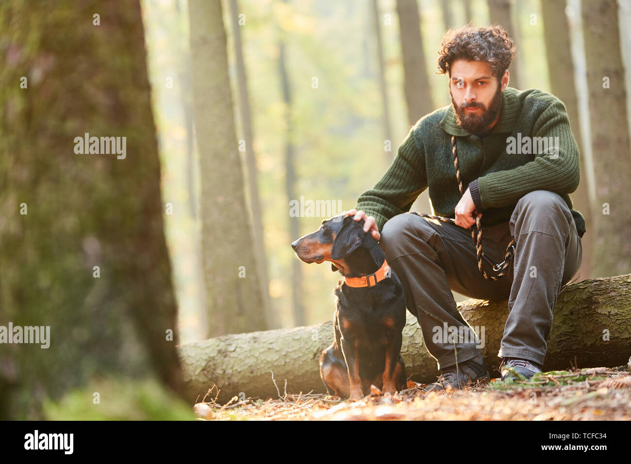 Forester è seduta su un log con un cane come un cane da caccia nei boschi Foto Stock
