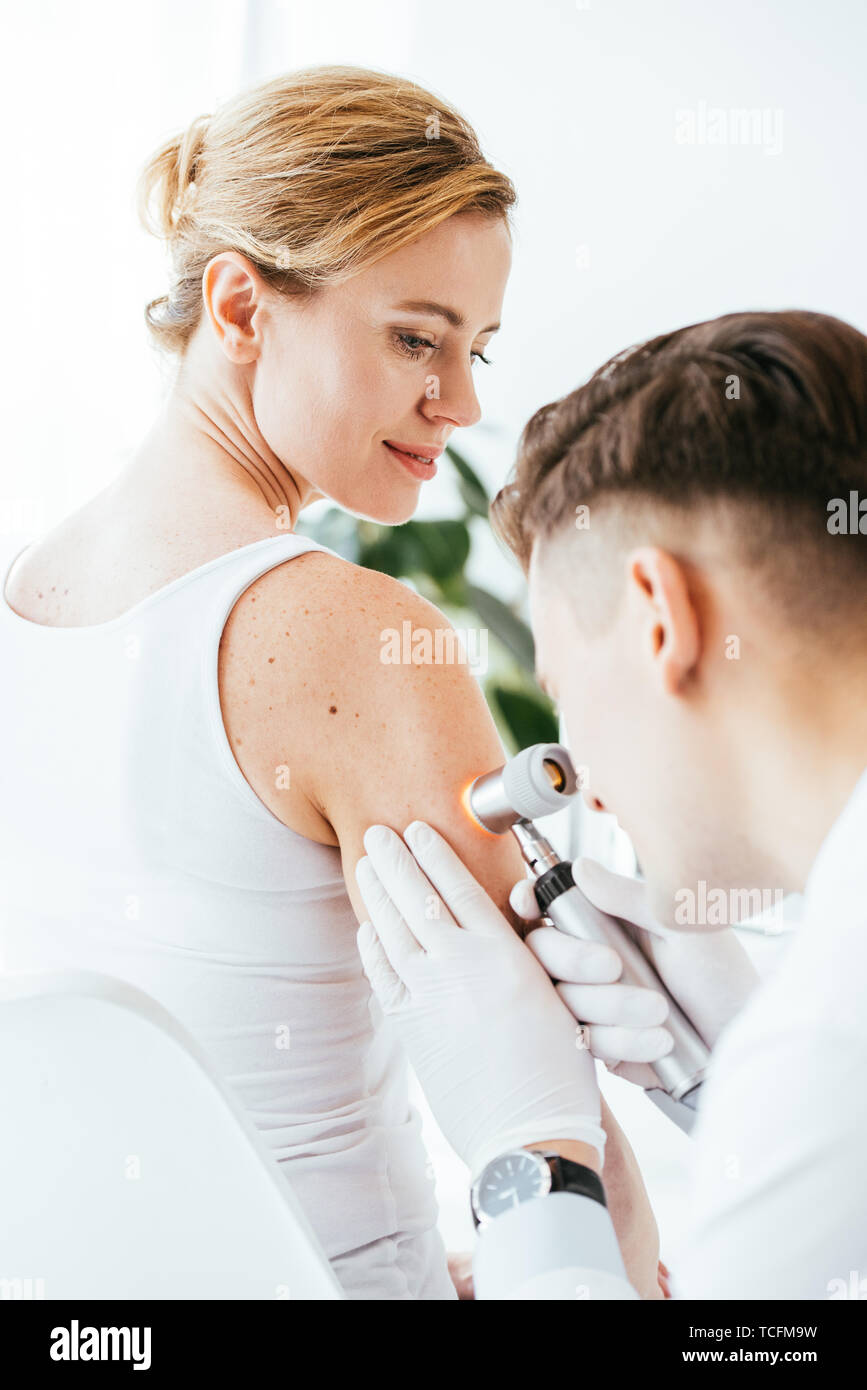 Il dermatologo in guanti in lattice azienda dermatoscope mentre esaminando bella paziente con malattia della pelle Foto Stock