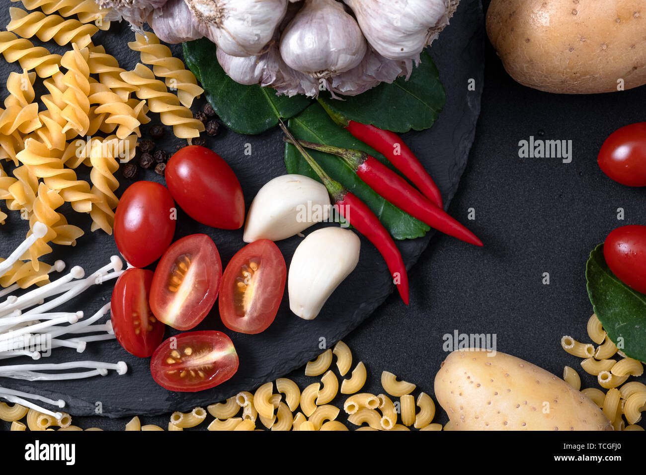 Vista dall'alto di ingredienti freschi. La cucina salutistica sfondo con verdura biologica e pasta per vegan su nero ardesia . Il pomodoro , Aglio fresco e chil Foto Stock
