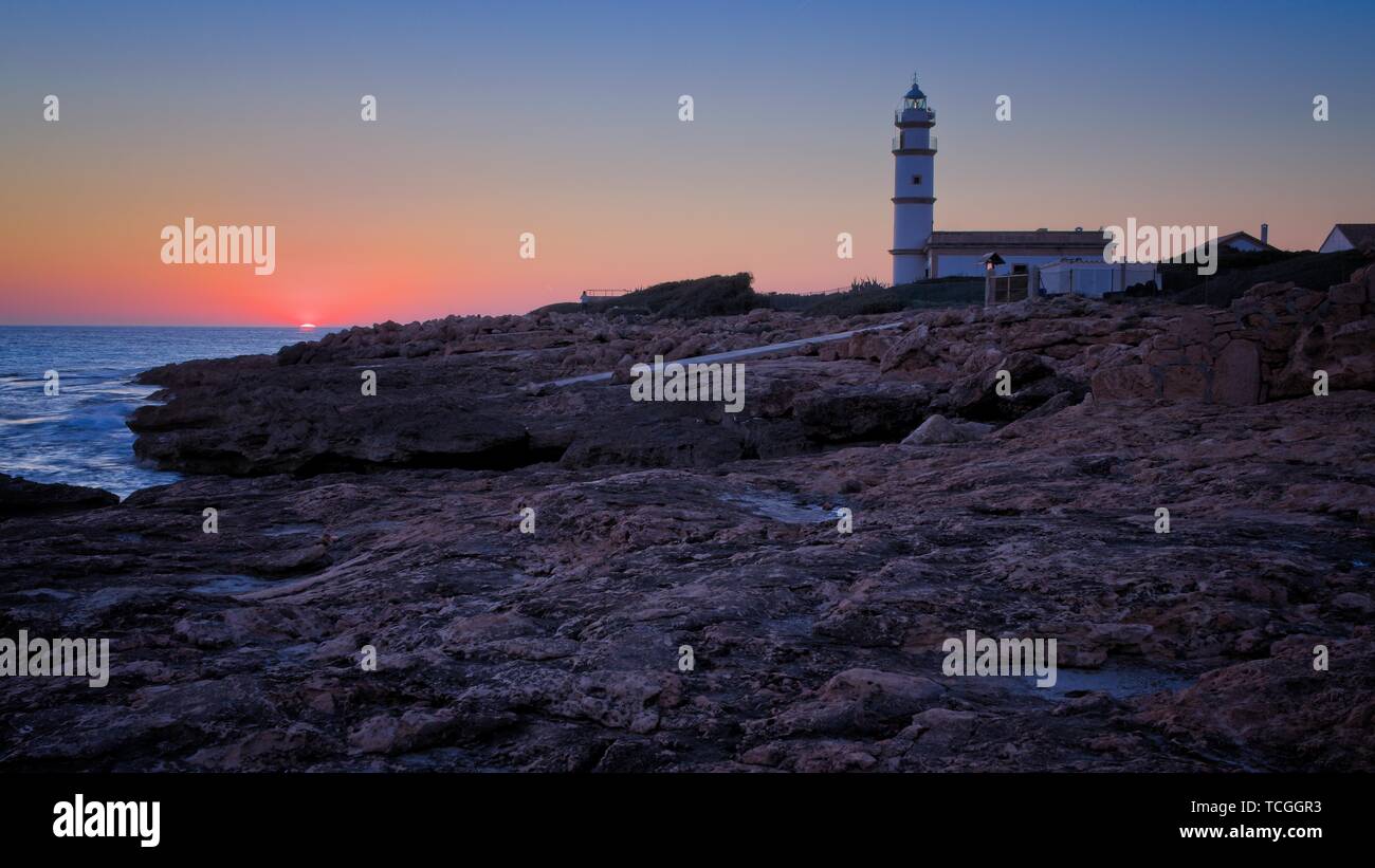 Faro lontano del cappuccio Ses Salines al tramonto, rocce, edificio, sole di setting, bello golden sky, Mallorca, Spagna. Foto Stock