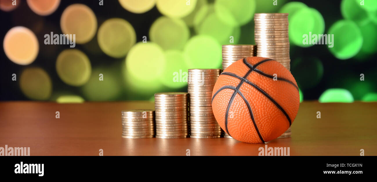 La pallacanestro e pile di monete d'oro nella crescita grafico sullo sfocato sfondo bokeh di fondo. Sport scommesse concept Foto Stock