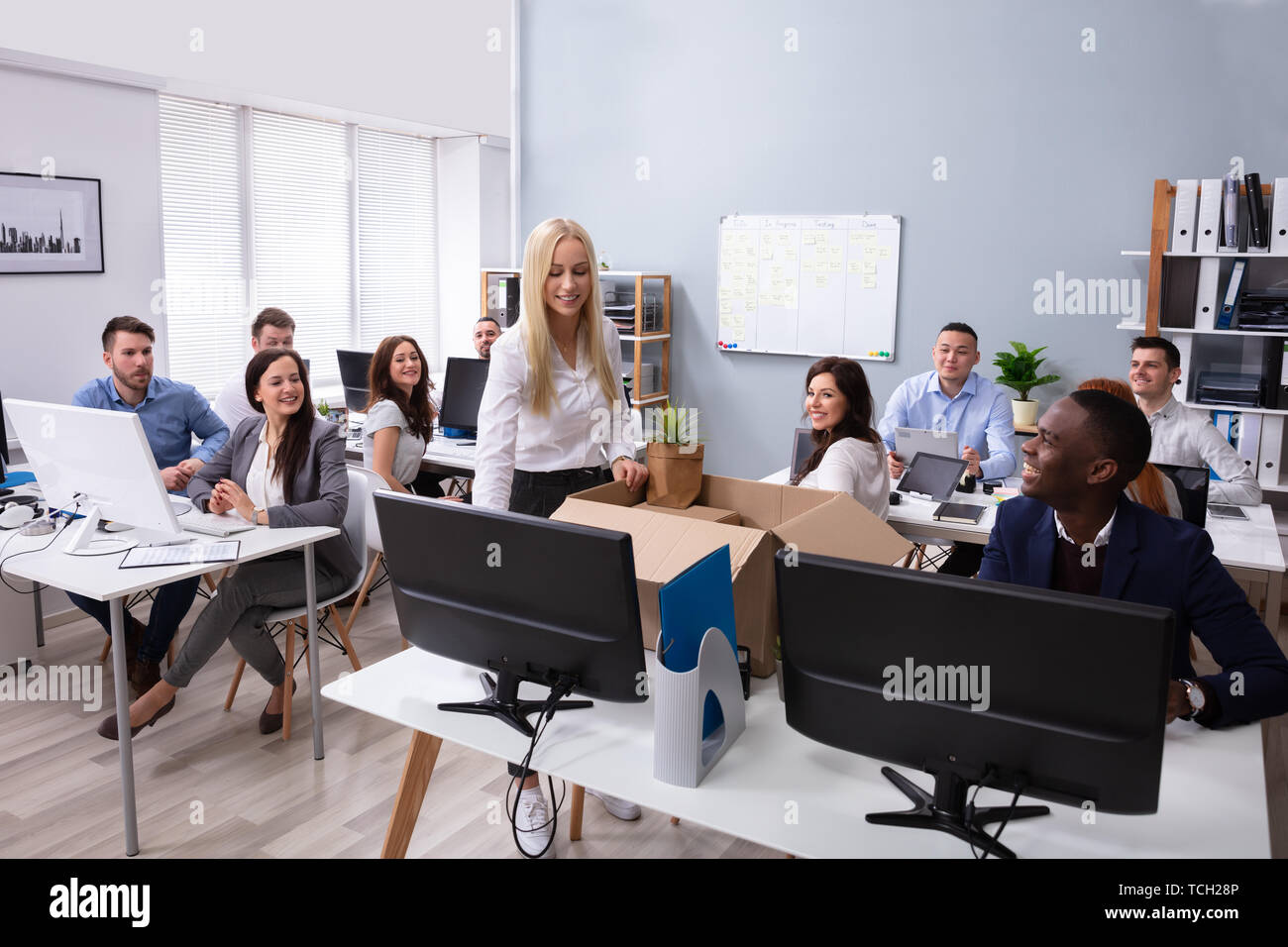 Gli imprenditori Guardando sorridente nuovo dipendente Disimballaggio Box con effetti personali in ufficio Foto Stock