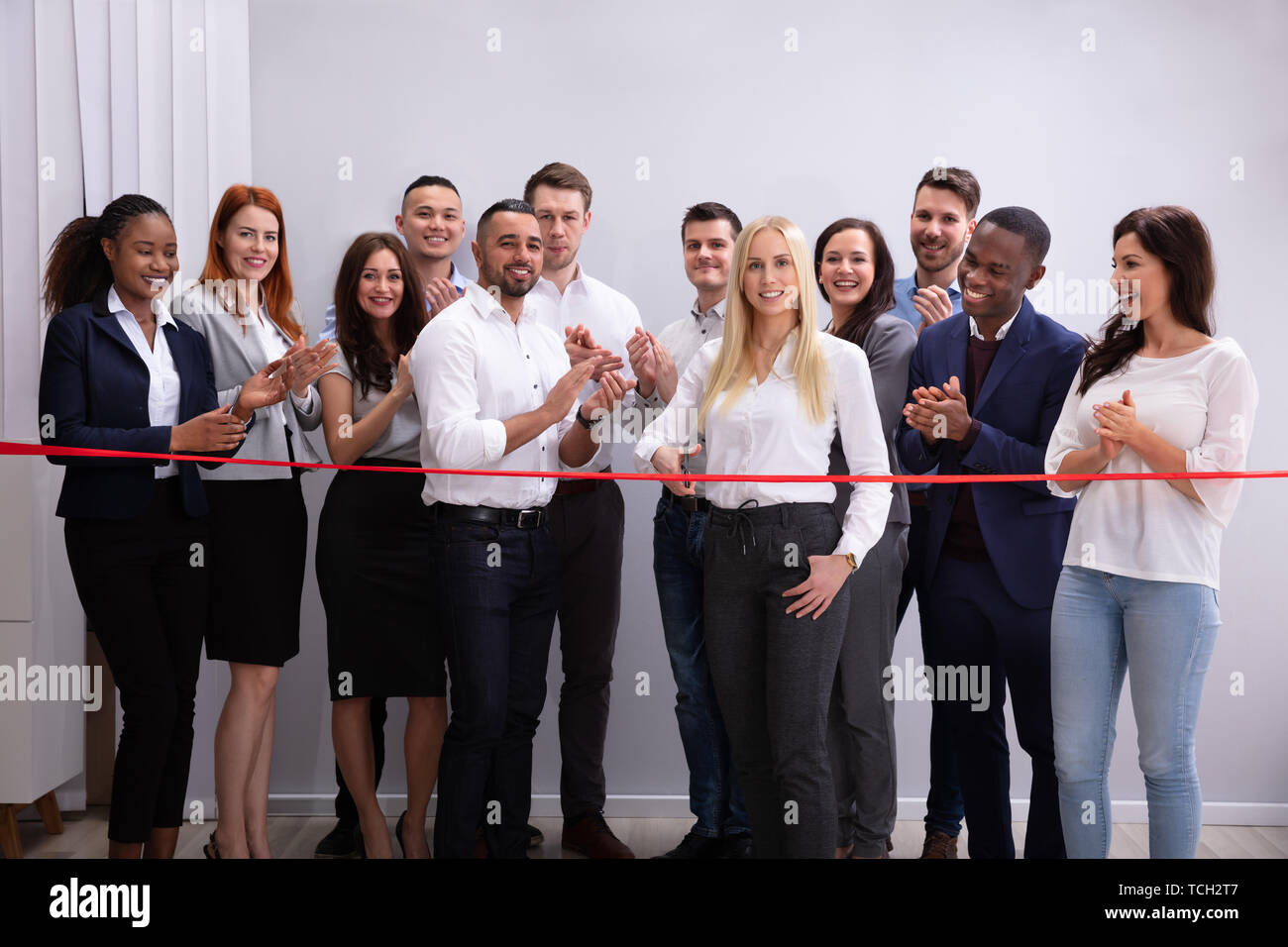 Sorridente Imprenditrice di successo per il taglio di un nastro rosso con il suo staff Foto Stock