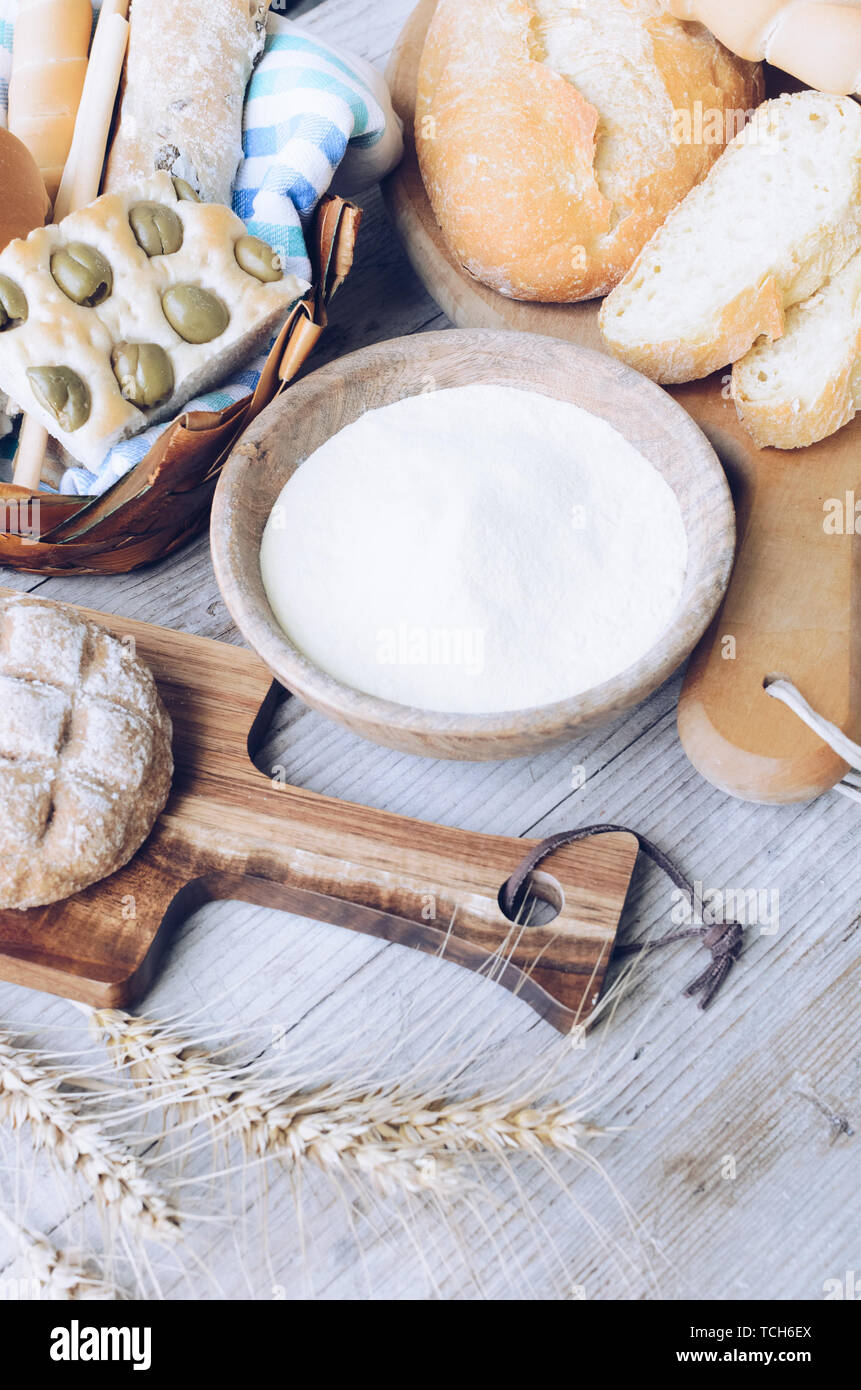 Diversi tipi di Italiano tradizionale di pane appena sfornato, vari tipi di pane e panini con ciotola di farina a fontana sul tavolo di legno dello sfondo. Rustico stile vintage. Foto Stock