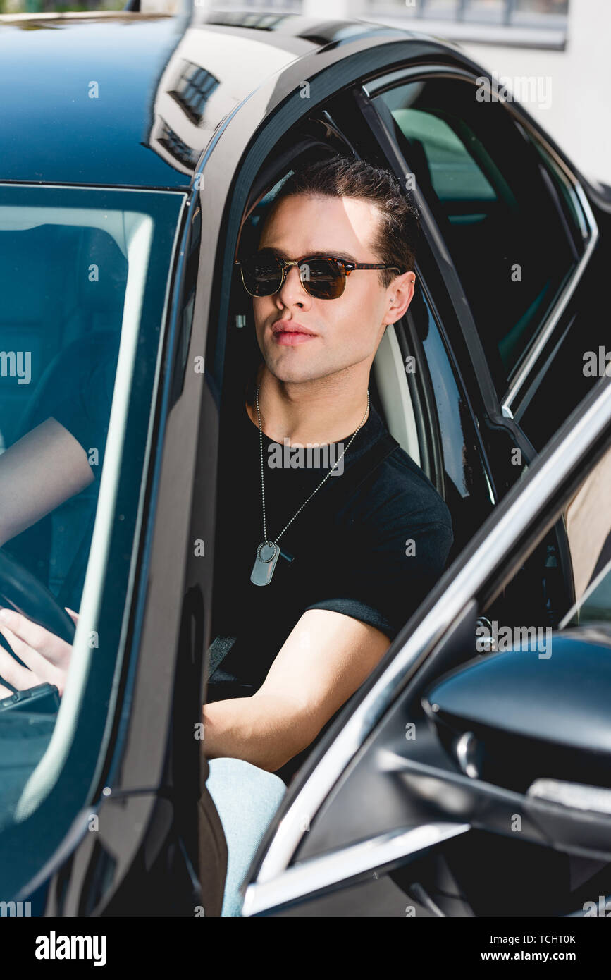 Bello elegante uomo in occhiali da sole con tag dog sitter in auto Foto Stock