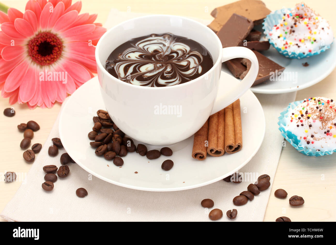 Tazza di caffè e gerbera, fagioli, bastoncini di cannella sul tavolo di legno Foto Stock