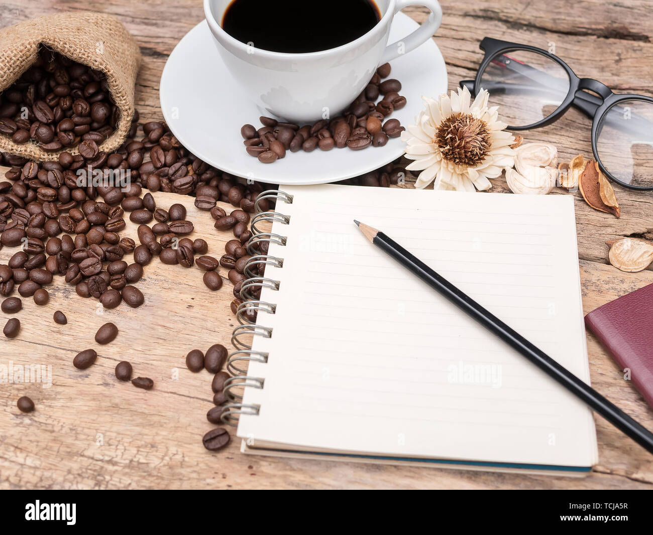 Tazza di caffè con chicco di caffè e notebook con una matita su un tavolo di legno. caffè menu sfondo per bar o caffetteria Foto Stock