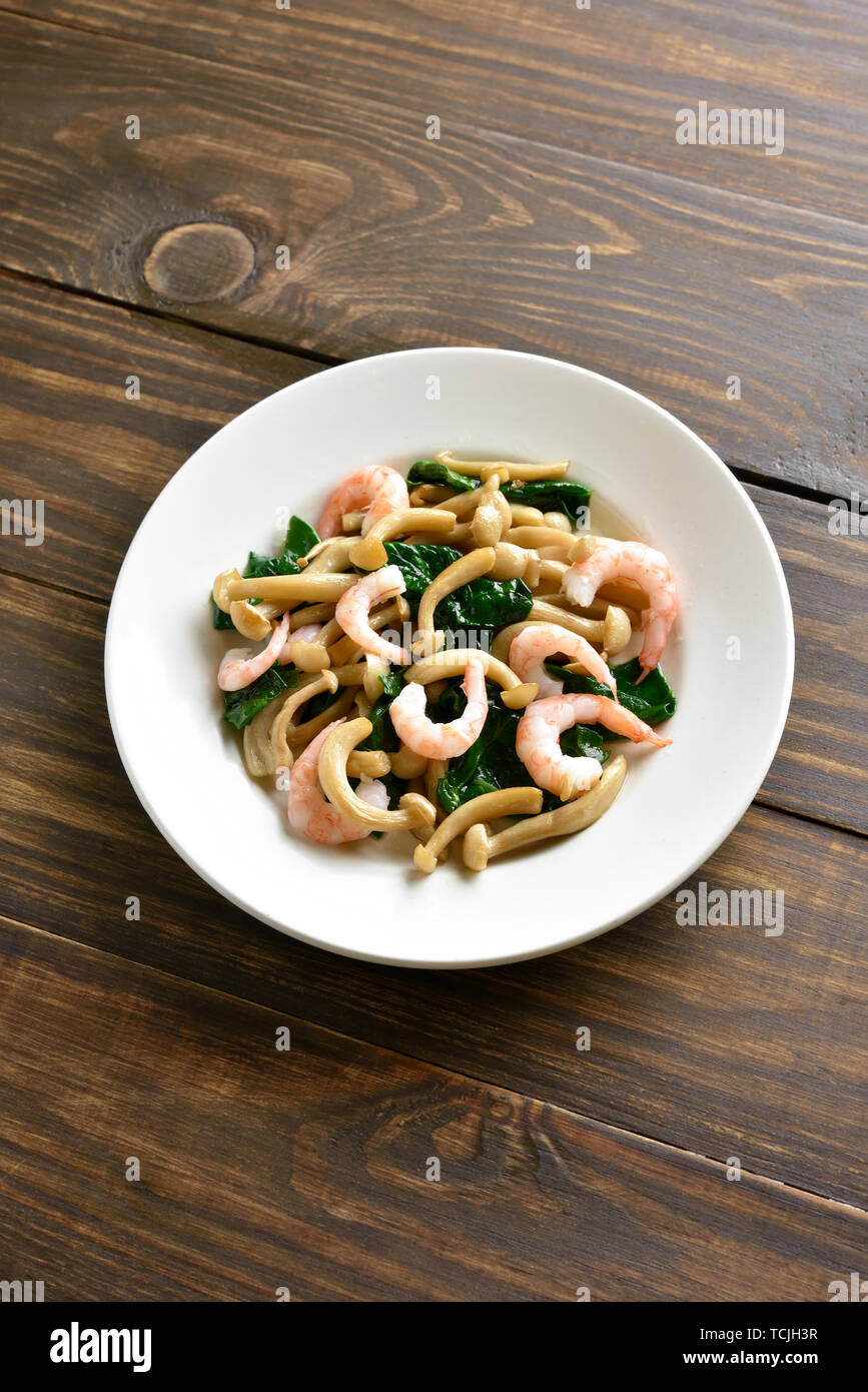 Stir-fried bianco di funghi di faggio con le foglie di spinaci e gamberetti su sfondo di legno con copia spazio. Foto Stock