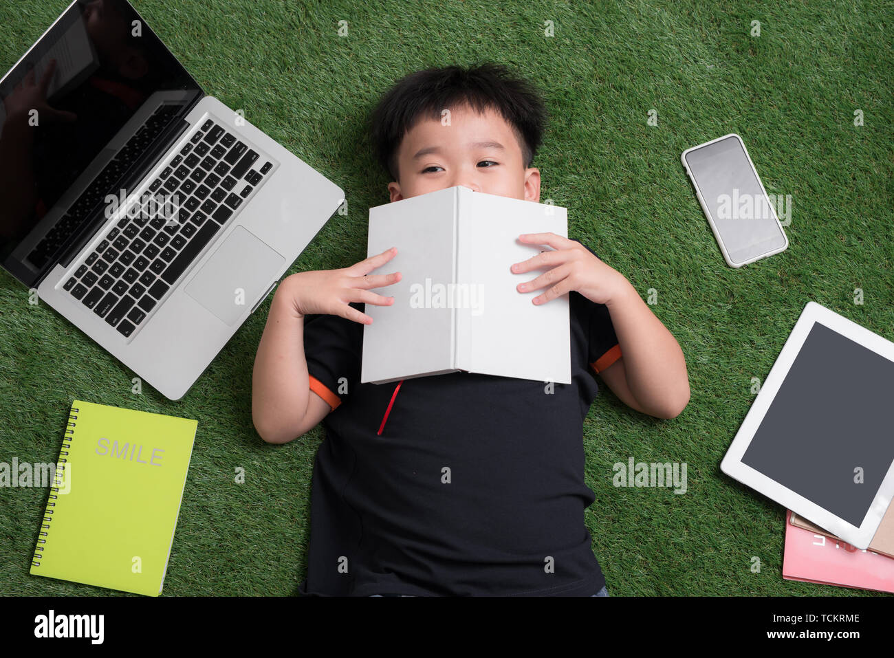 A sette anni di età bambino leggendo un libro sdraiati sull'erba Foto Stock