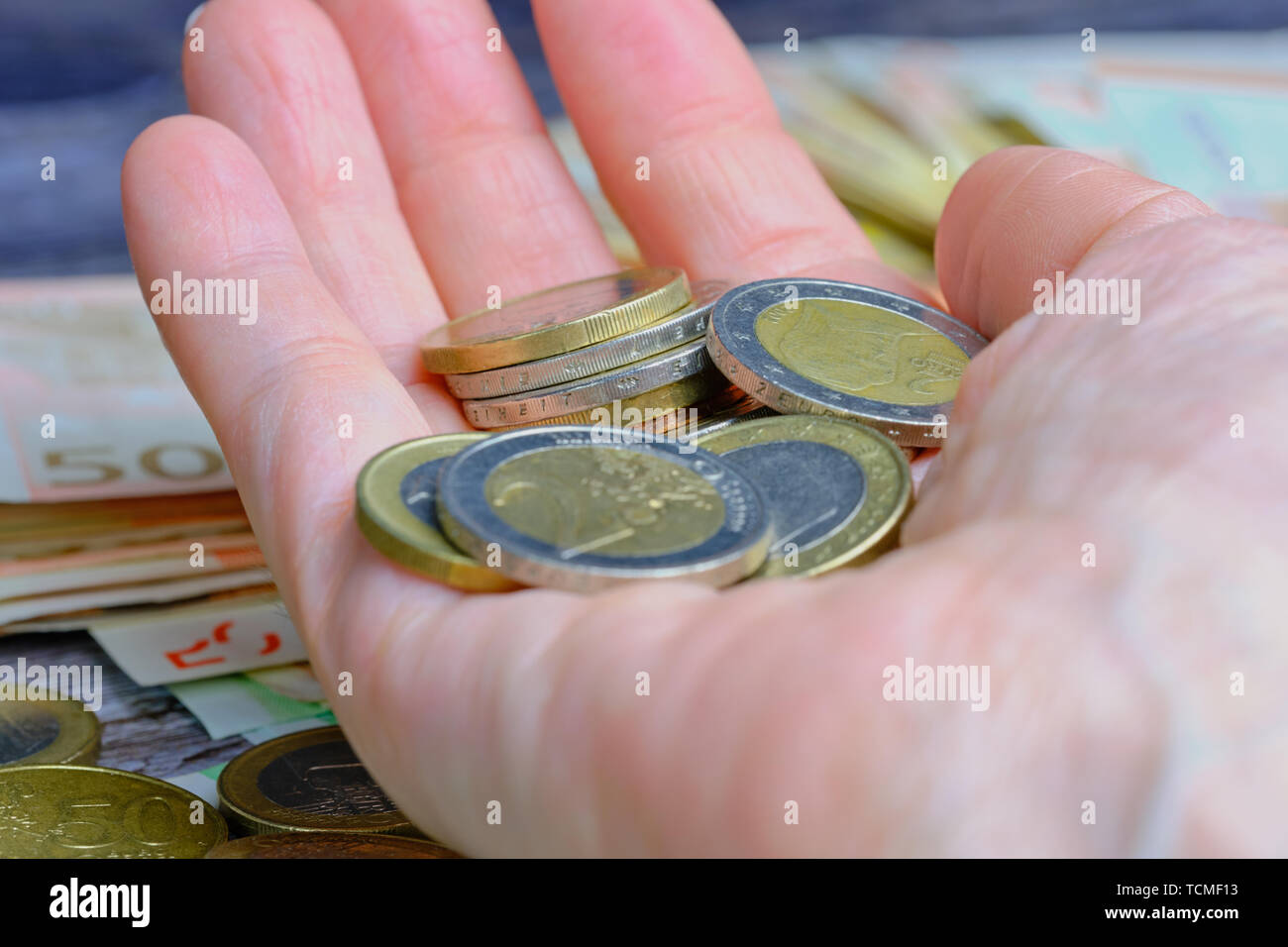 Femmina tenuta a mano uno e due monete in euro, intorno sono disposte le banconote e le monete in euro Foto Stock