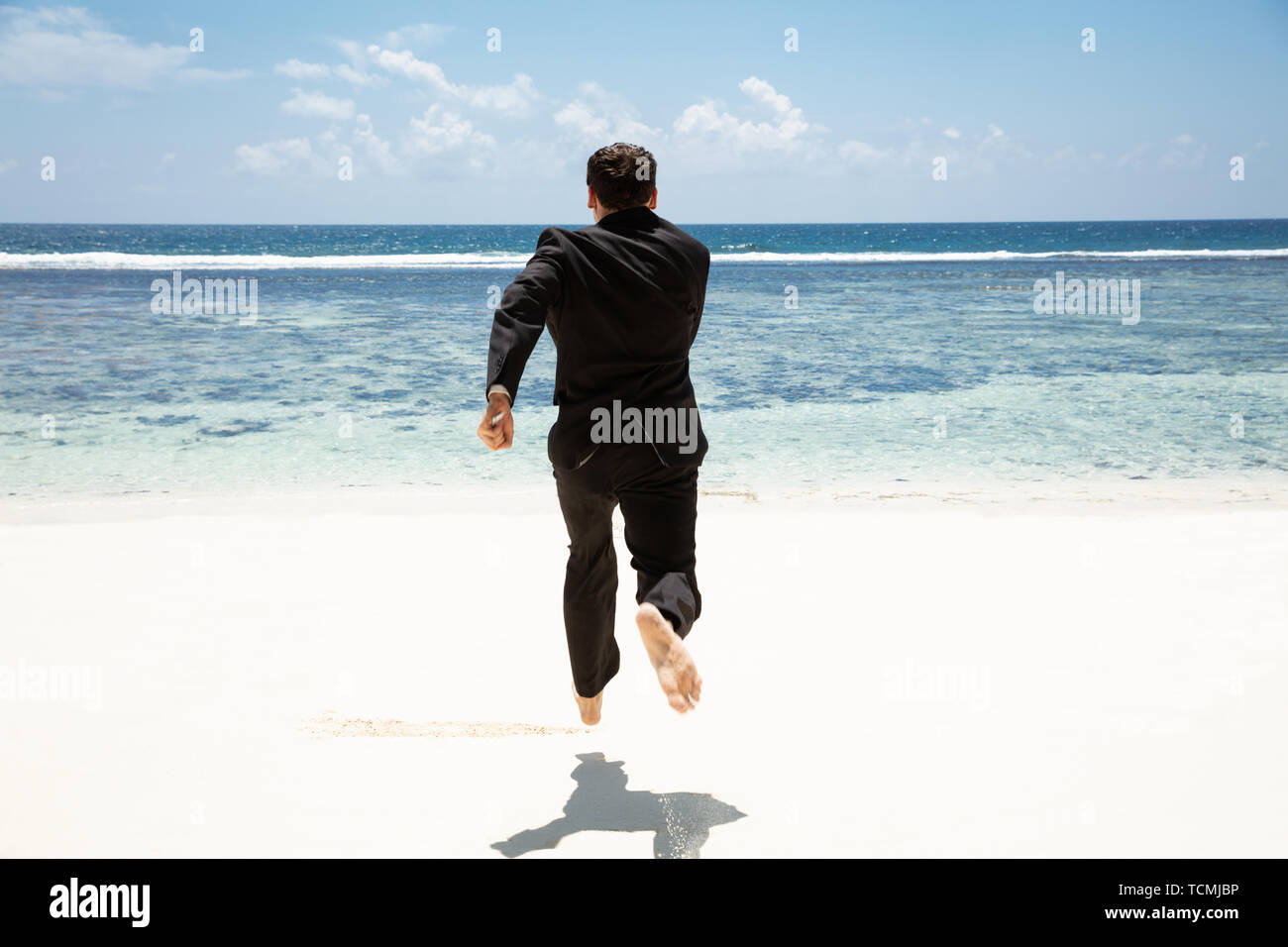 Vista posteriore di un imprenditore correre a piedi nudi verso il mare idilliaco in spiaggia Foto Stock