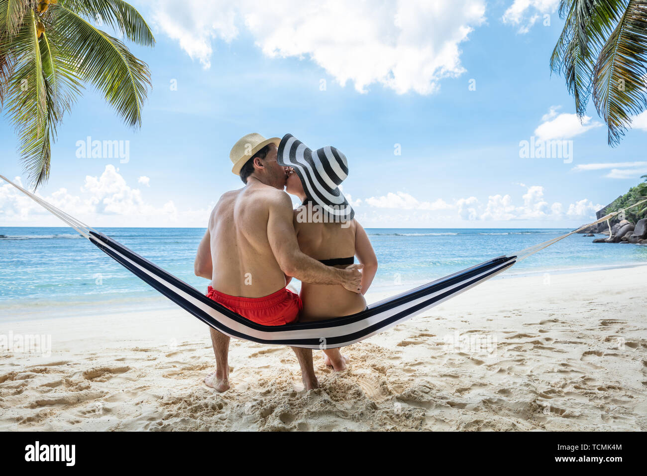 Vista posteriore della coppia giovane seduto su amaca Kissing vicino al mare sulla spiaggia Foto Stock
