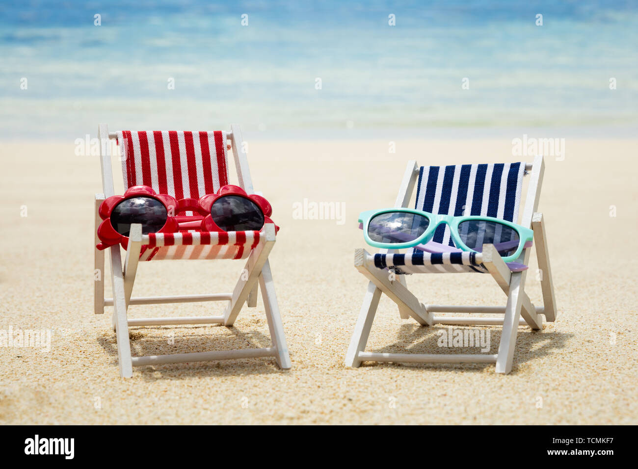 Due tipi di rosso e blu Occhiali da sole sulla sedia a sdraio sulla sabbia in spiaggia Foto Stock