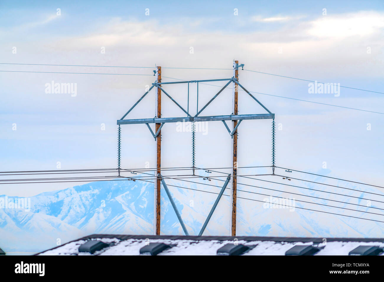 Linee di alimentazione aeree con la montagna innevata e la nuvola riempì sfondo cielo Foto Stock