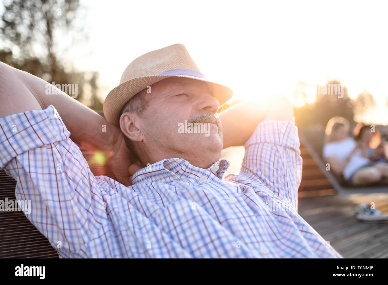 Il vecchio uomo ispanico si siede sul banco, sorridente, godendo di estate giornata di sole. Foto Stock