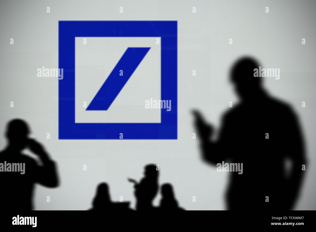 La Deutsche Bank ha il logo è visibile su uno schermo a LED in background mentre si profila una persona utilizza uno smartphone in primo piano (solo uso editoriale) Foto Stock