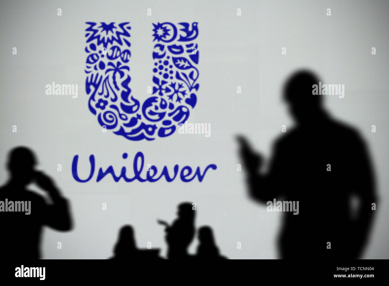 La Unilever logo è visibile su uno schermo a LED in background mentre si profila una persona utilizza uno smartphone in primo piano (solo uso editoriale) Foto Stock