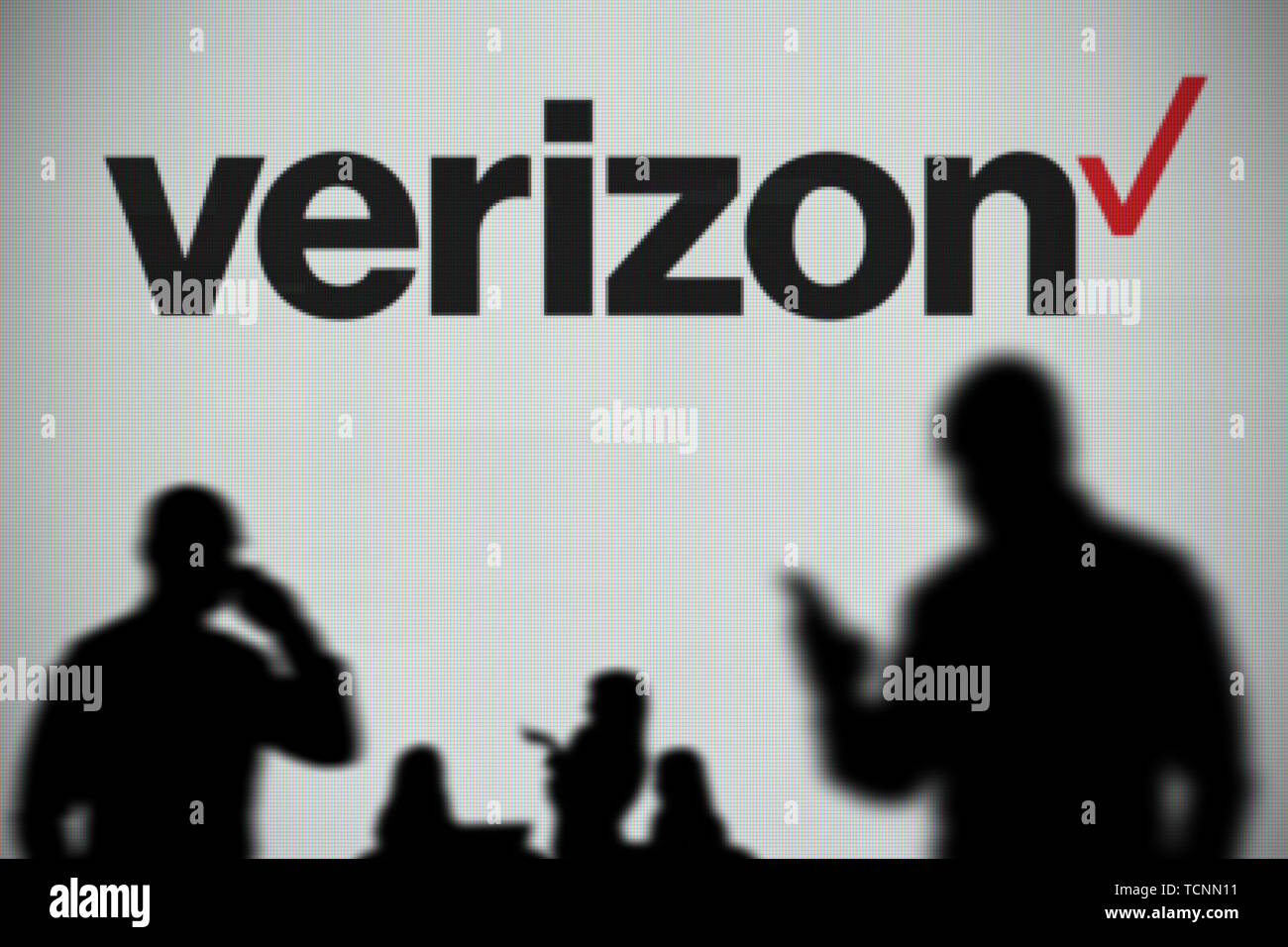 Il logo Verizon è visto su uno schermo a LED in background mentre si profila una persona utilizza uno smartphone in primo piano (solo uso editoriale) Foto Stock