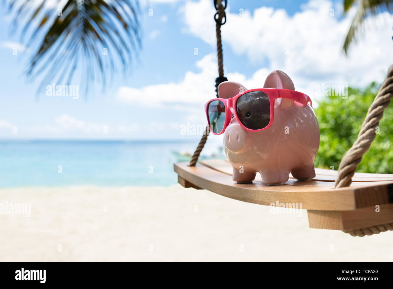 Close-up di Rosa Piggybank con gli occhiali da sole sul brandeggio in legno a Beach Foto Stock