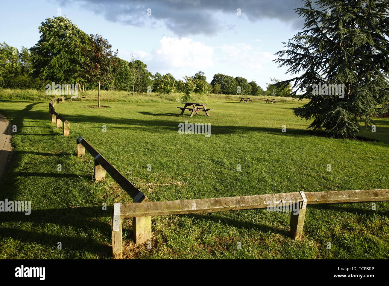Una panchina nel parco e lungo in legno recinzione bassa nella tarda sera di luce con lunghe ombre. Foto Stock