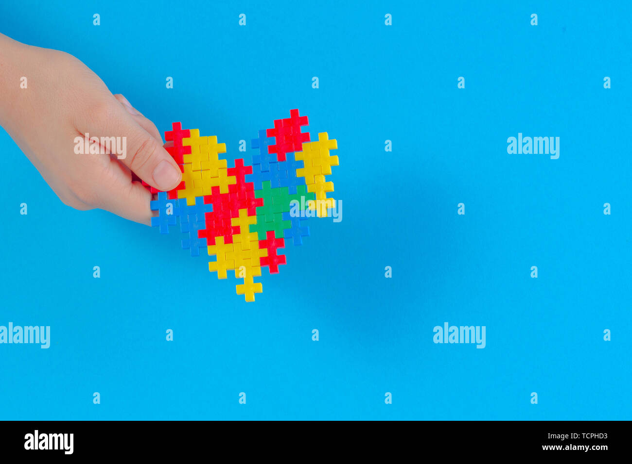 Bambino mano azienda cuore colorati su sfondo blu. Mondo autismo consapevolezza giorno di concetto Foto Stock