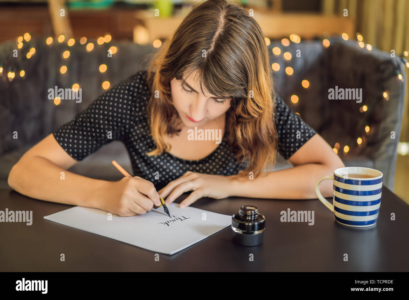La ringrazio. Calligrapher giovane donna scrive una frase sul libro bianco. Inscrivendo ornamentali in lettere decorate. La calligrafia, graphic design, scritte Foto Stock
