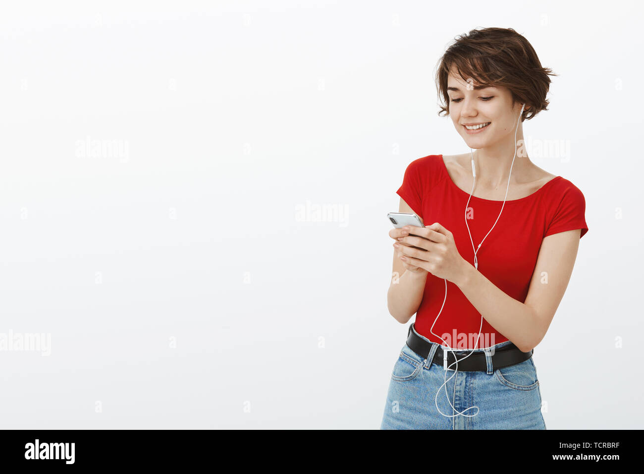 Guardare la ragazza vide il concerto di musica luogo pubblico indossare gli auricolari dello smartphone in attesa con gioia sorridente cellulare schermo display rendendo song playlist utilizzando app Foto Stock
