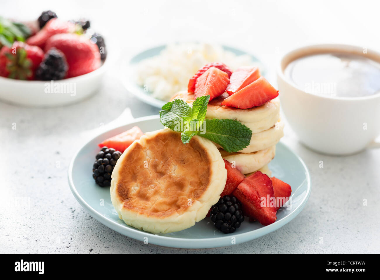 Cottage cheese pancakes syrniki con frutti di bosco freschi e la tazza di caffè. Una gustosa colazione sana cibo Foto Stock