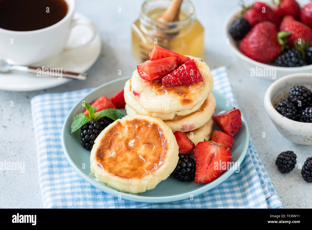 Cottage cheese pancakes syrniki con Fragola, blackberry e miele sulla piastra di blu. Una gustosa colazione sana Foto Stock