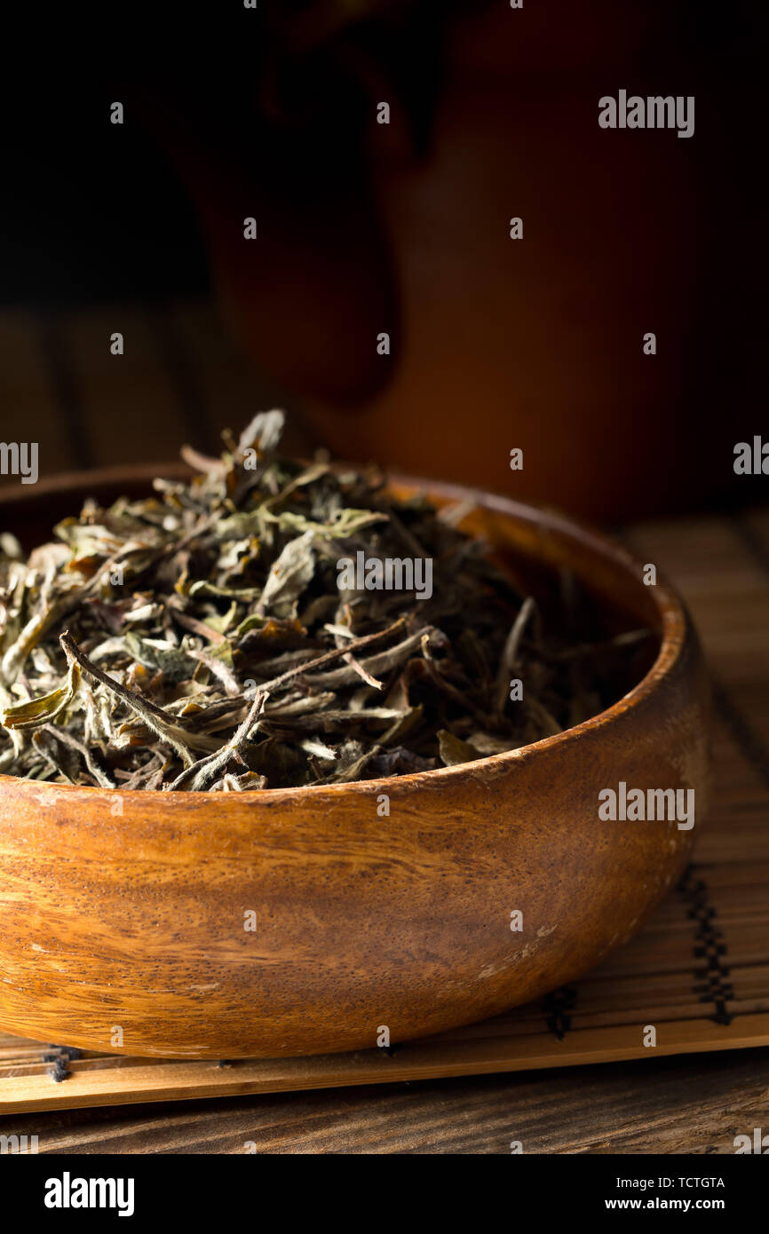 Cumulo di essiccato, crudo Tè bianco lascia nella ciotola di legno sul tappetino di bambù sfondo Foto Stock
