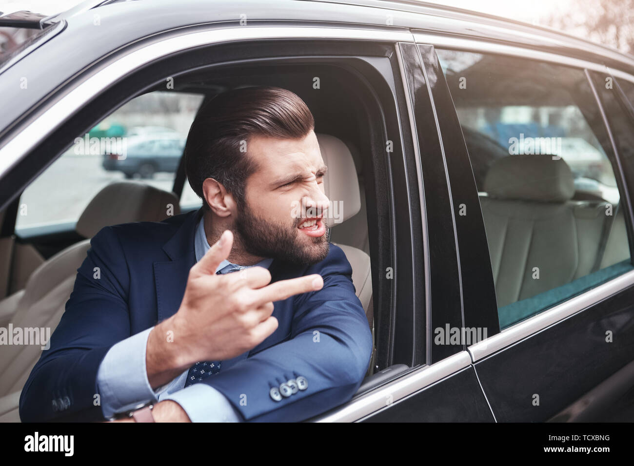 Rude imprenditore. Arrabbiato e rude barbuto imprenditore nel formale di usura è gesticolando e facendo una grimace mentre alla guida della sua auto. Le emozioni negative. Busine Foto Stock
