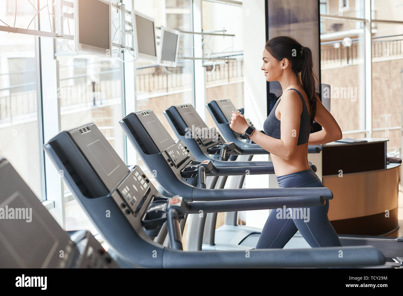 Miglioramento del corpo. Vista laterale della giovane e bella donna di abbigliamento sportivo in esecuzione su un tapis roulant in palestra. Allenamento cardio. Sport e fitness concetto. Healt Foto Stock