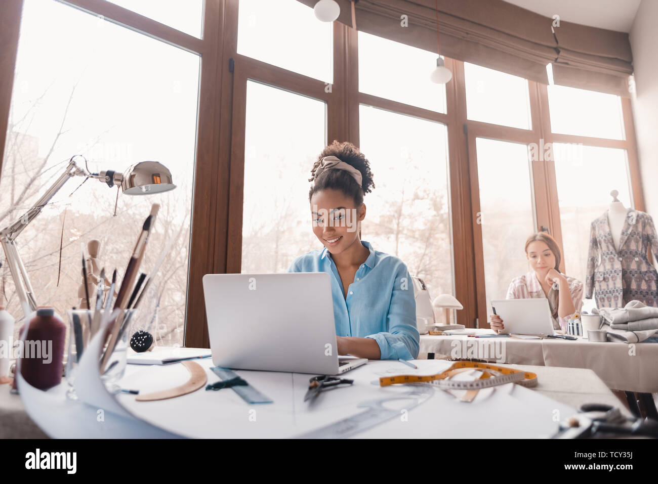 Tenendo il divertimento in studio di design. Due giovani donne attraenti a lavorare su un nuovo progetto di design. Giovane donna africana in primo piano e caucasico uno alla Foto Stock