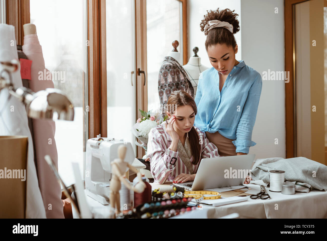 Si aiutano a vicenda con il progetto. Close-up di due giovani donne attraenti a lavorare su un nuovo progetto di design. Giovane donna africana in primo piano e cauc Foto Stock