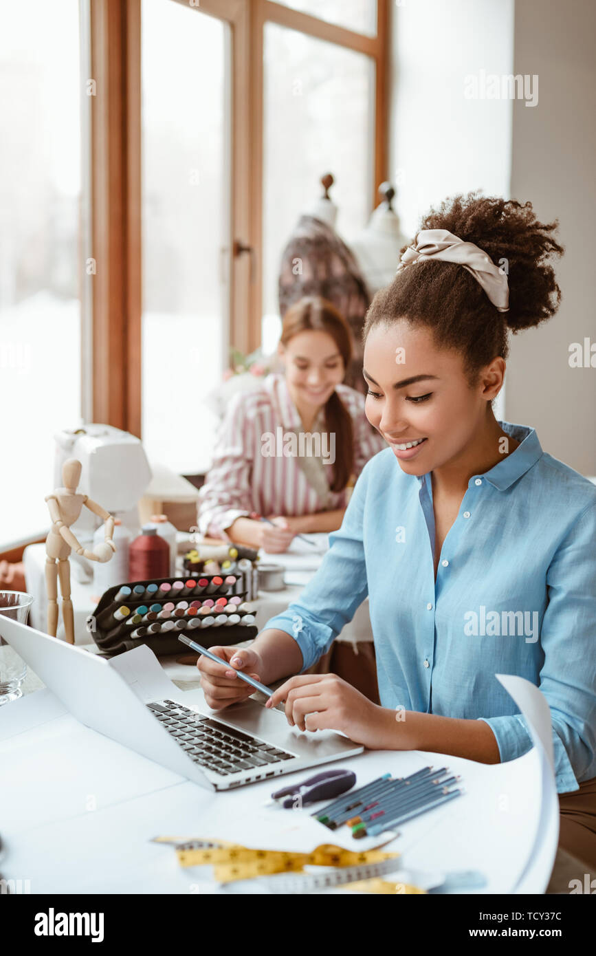 Tenendo il divertimento in studio di design. Due giovani donne attraenti a lavorare su un nuovo progetto di design. Giovane donna africana in primo piano e caucasico uno alla Foto Stock