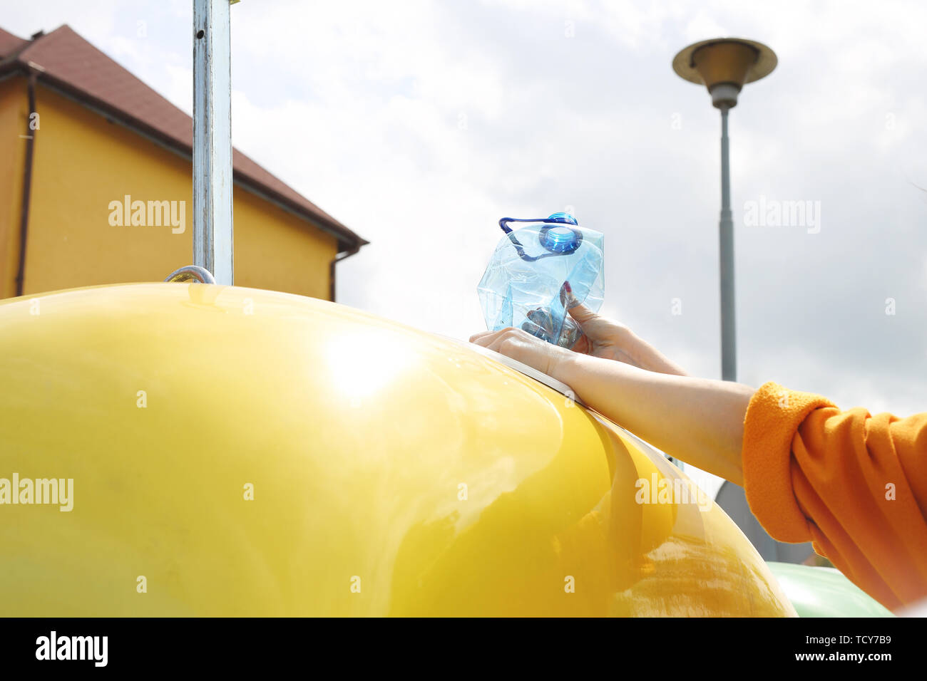 Riciclaggio di una donna getta rifiuti di plastica in un contenitore giallo Foto Stock