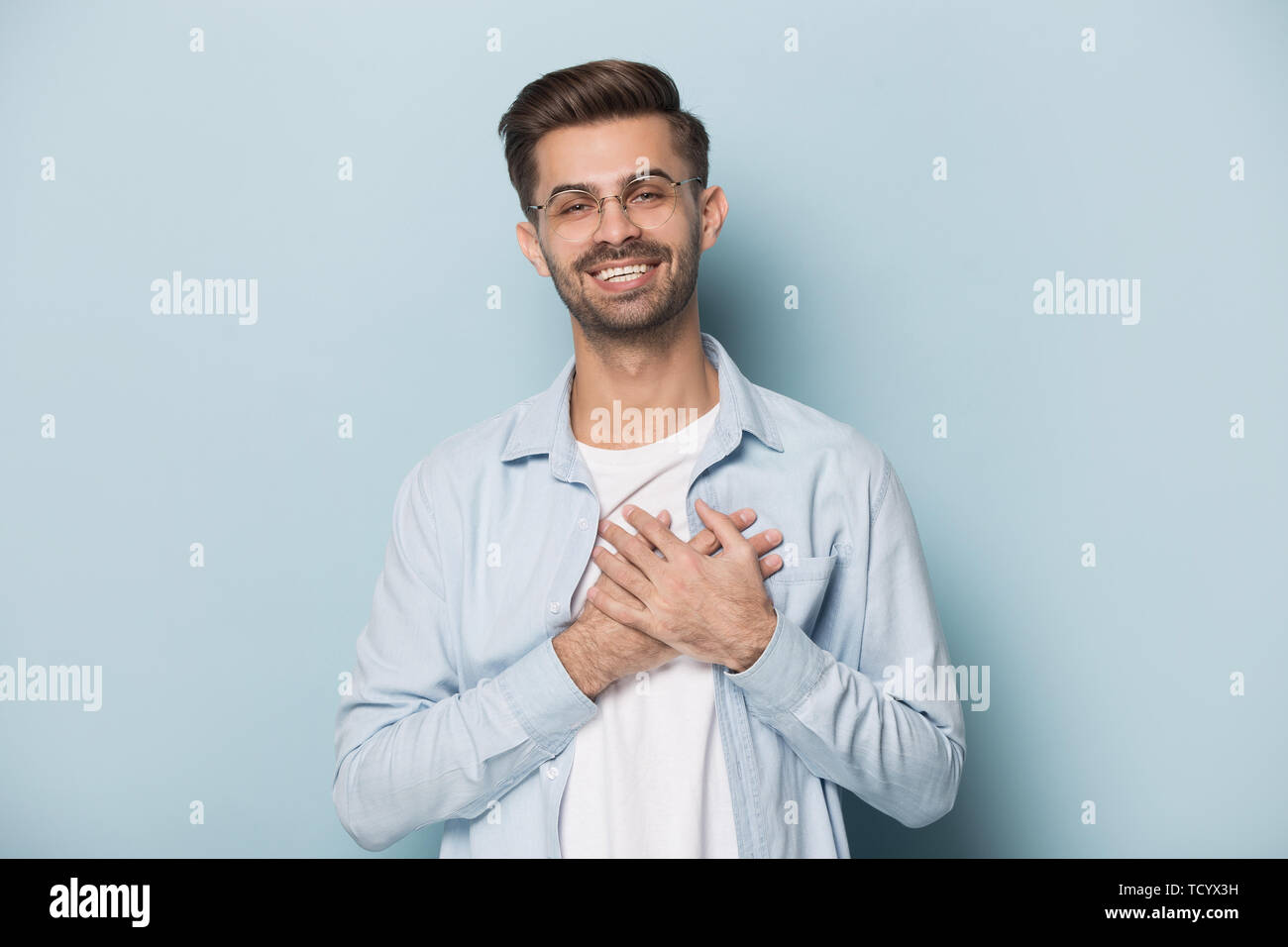 Grato guy in bicchieri mettere le mani sul petto studio shot Foto Stock