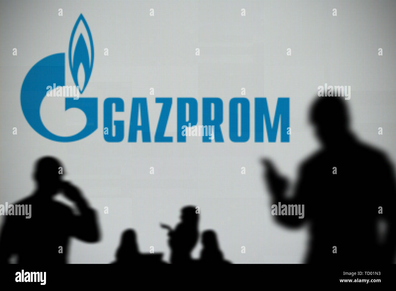 Il logo di Gazprom è visto su uno schermo a LED in background mentre si profila una persona utilizza uno smartphone in primo piano (solo uso editoriale) Foto Stock
