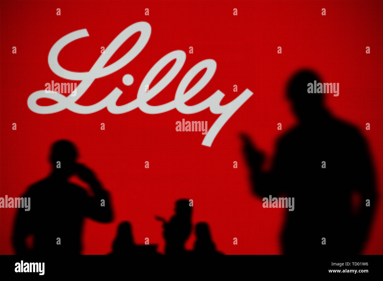 La Eli Lilly logo è visibile su uno schermo a LED in background mentre si profila una persona utilizza uno smartphone in primo piano (solo uso editoriale) Foto Stock