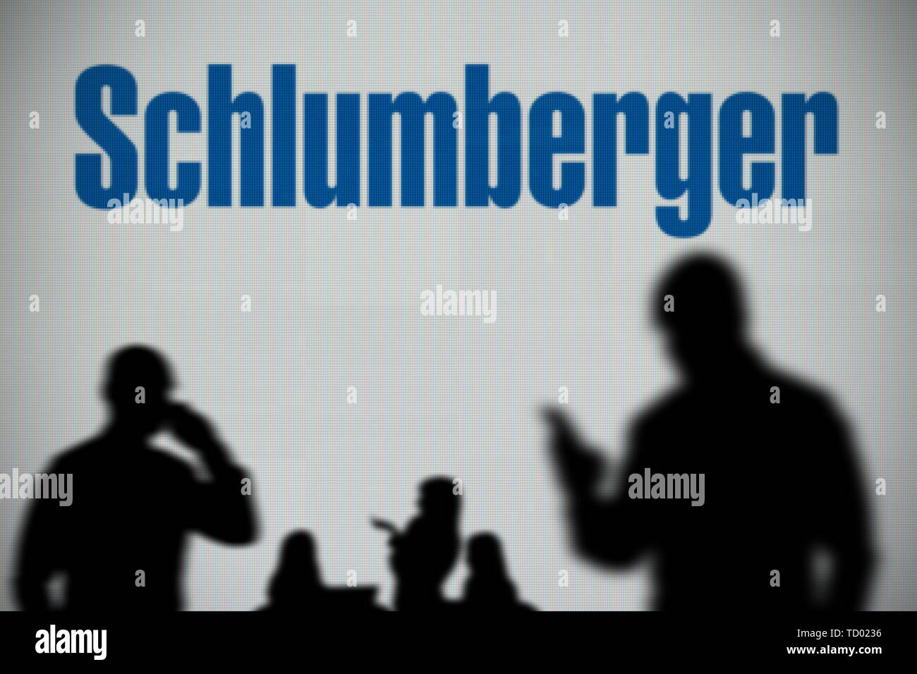 La Schlumberger logo è visibile su uno schermo a LED in background mentre si profila una persona utilizza uno smartphone in primo piano (solo uso editoriale) Foto Stock