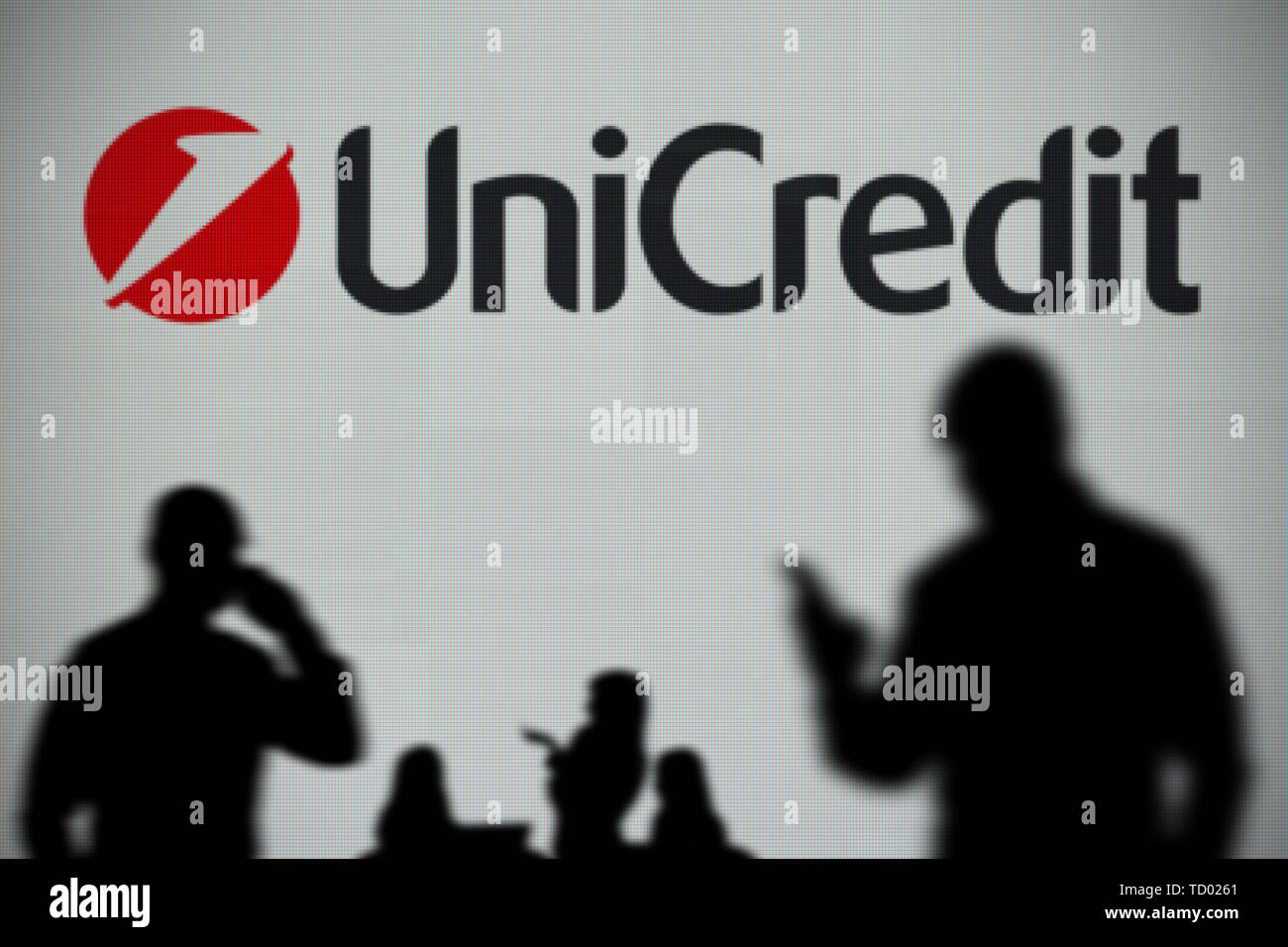 Il logo UniCredit è visto su uno schermo a LED in background mentre si profila una persona utilizza uno smartphone in primo piano (solo uso editoriale) Foto Stock