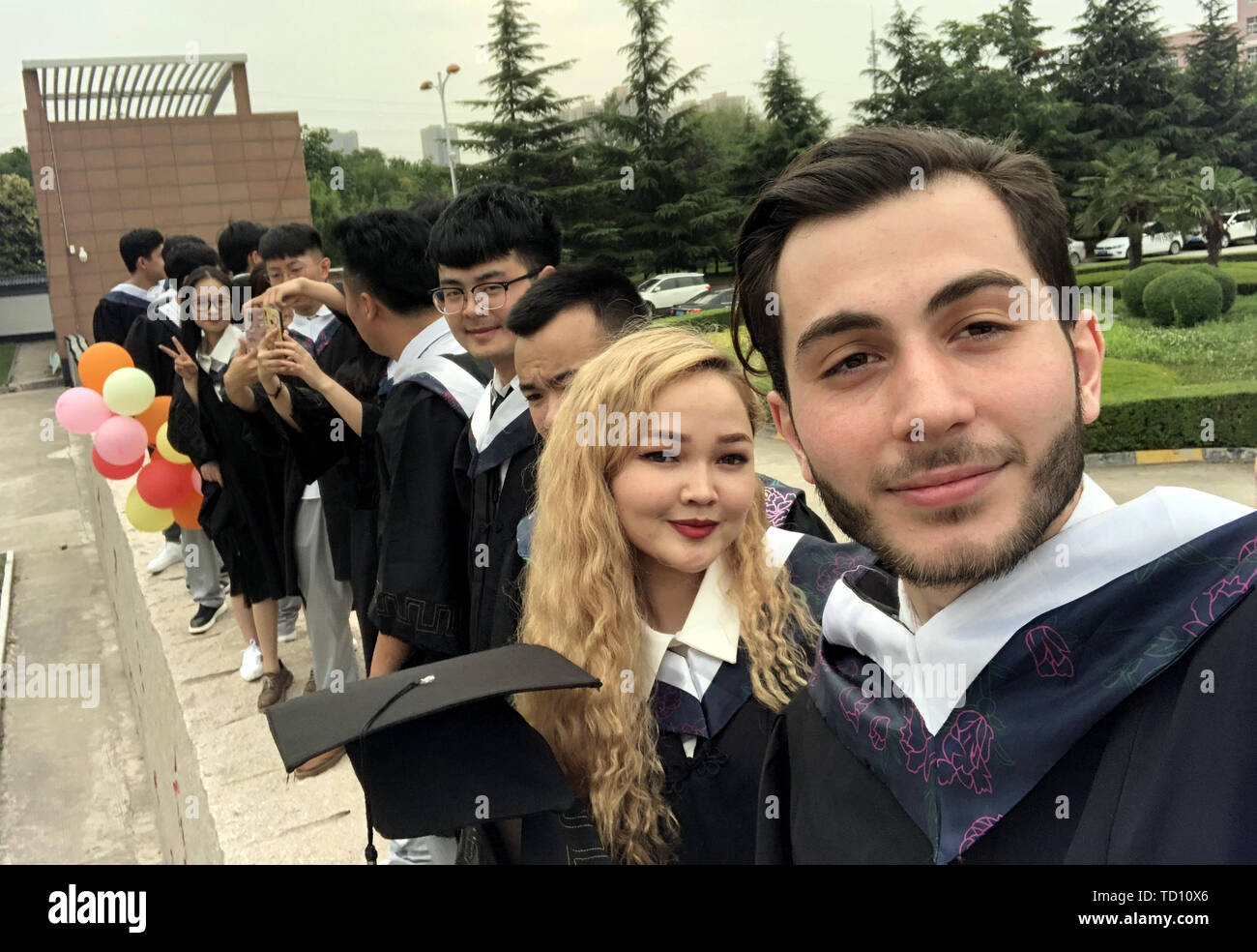 (190611) -- Xi'an, 11 giugno 2019 (Xinhua) -- Aushev Djamaleil (R) prende un selfie con i suoi compagni di scuola in abito accademico in Shaanxi Università di Medicina Cinese in Cina nord-occidentale della provincia di Shaanxi, 11 giugno 2019. Aushev Djamaleil, un Kazakhstani da studente della Scuola Internazionale di Educazione in Shaanxi università di medicina cinese, ha quasi finito i suoi studi universitari in agopuntura e moxibustione e massaggi, e proseguirà il suo grado di maestro nella stessa principali. Egli vuole che la medicina tradizionale cinese, attraverso i suoi sforzi, possono essere applicati a più pazienti nel suo paese di origine. Un tot Foto Stock