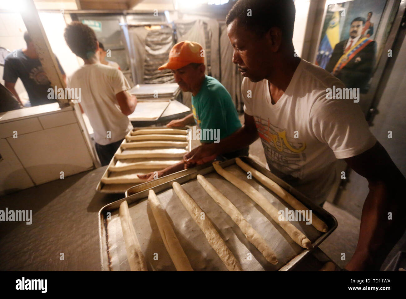 05 giugno 2019, Venezuela, Caracas: i dipendenti portano vassoi da forno con baguette in 'La Minka', un panificio gestito da Maduro sostenitori del governo. Sullo sfondo si può vedere un poster con una foto del presidente. L'ex panificio privato è stato chiamato 'Mansion's Bakery'. Ora circa 6.000 pezzi di pane sono prodotte ogni giorno a prezzi fissati dallo stato. Il paese con la più grande riserva di petrolio nel mondo è in un drammatico declino. La svalutazione del denaro è il più alto del mondo, per molte persone il cibo è insostenibile. Questi "' Bolivariana panetterie, che vendono il pane a prezzi fissi, vedere loro ta Foto Stock