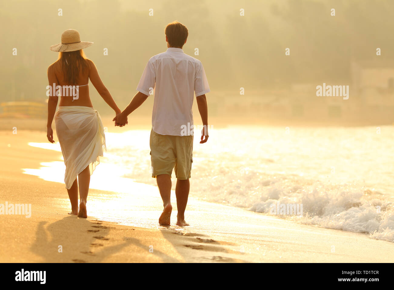 Vista posteriore di una giovane azienda mani di camminare sulla spiaggia di sunrise Foto Stock