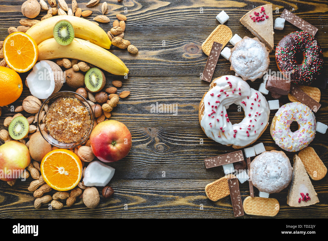Malsano e dolci sani su sfondo di legno. Organici e prodotti alimentari dietetici e il problema del rifiuto da dessert nocivi. Frutta e noci vs ciambella Foto Stock