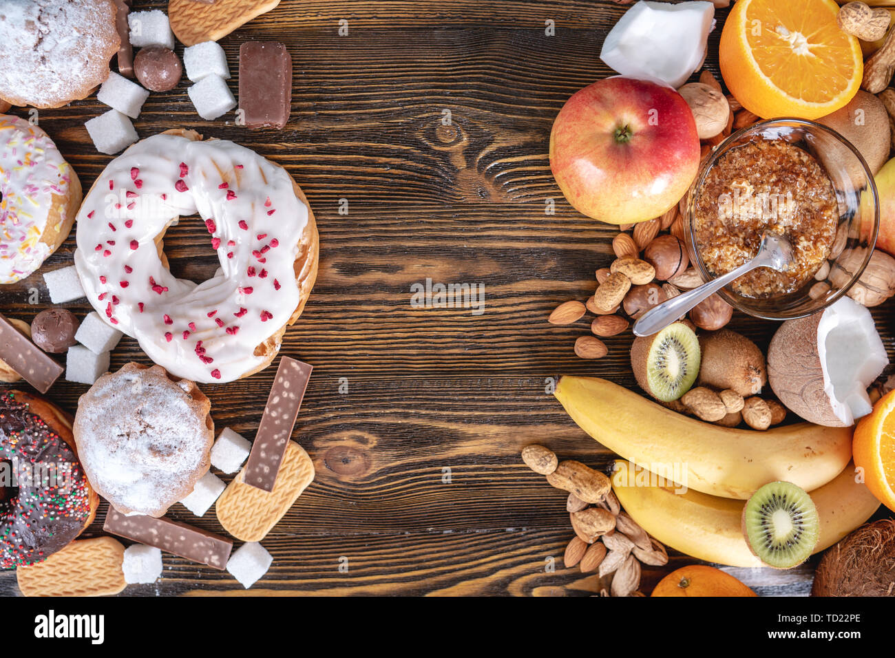 Malsano e dolci sani su sfondo di legno. Organici e prodotti alimentari dietetici e il problema del rifiuto da dessert nocivi. Frutta e noci vs ciambella Foto Stock