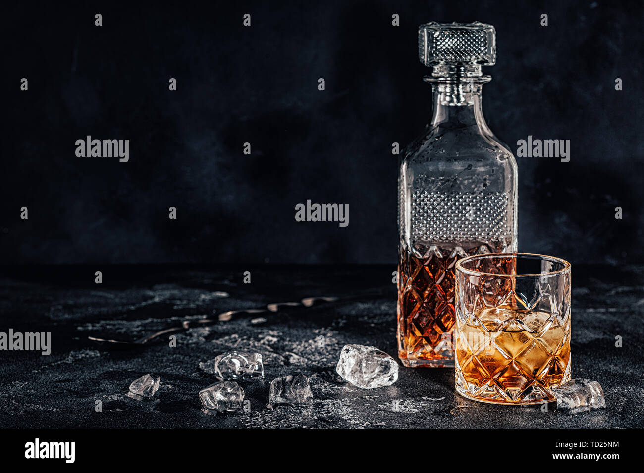 Bicchiere di whiskey con un decantatore quadrato su una pietra nera dello sfondo. Foto Stock