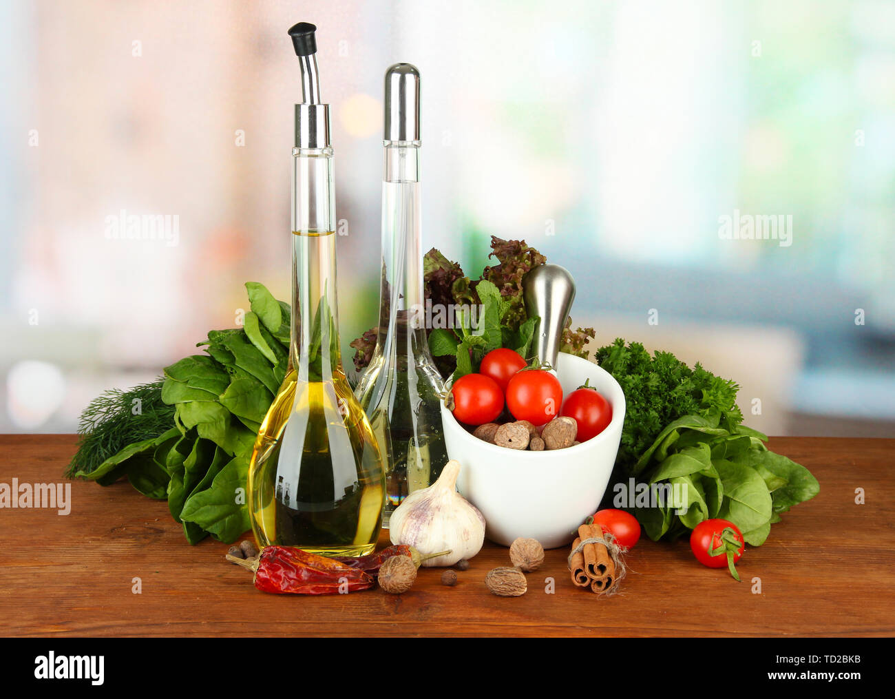 Composizione del mortaio, bottiglie con olio di oliva e aceto, e verde erboristeria, su sfondo lucido Foto Stock